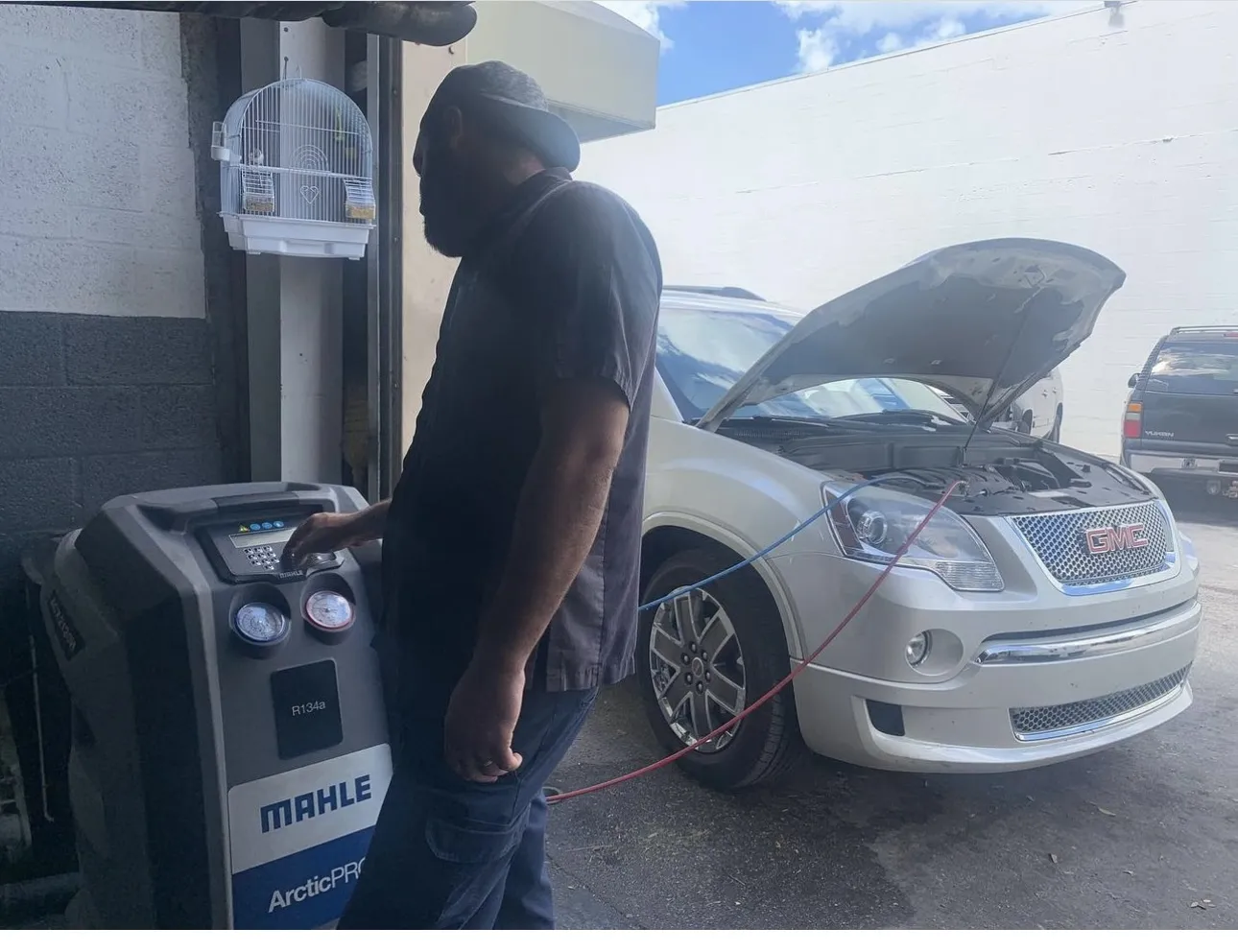 A mechanic running an A/C service machine on a white car